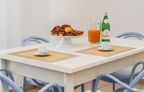 Ein Esstisch mit weißer Tischdecke, ein Tablett mit Gebäck, ein Glas Orangensaft und eine Flasche Acqua Panna.