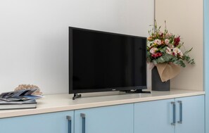 Ein Flachbildfernseher auf einem hellen Schrank, daneben ein Blumenstrauß.
