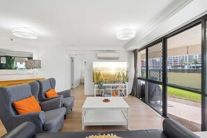 A modern living room with a sofa, coffee table, and a view through large windows. - Victoria on Broadbeach (Broadbeach)
