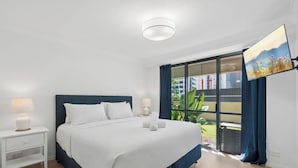 Een moderne hotelkamer met een groot bed, een nachtkastje, een televisie en een balkon met uitzicht op de stad.