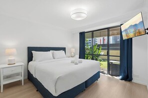 A modern hotel room with a large bed, a nightstand, a TV, and a balcony with a city view. - Victoria on Broadbeach (Broadbeach)