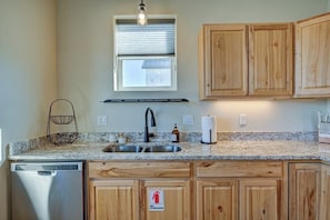 A kitchen with wooden cabinets, a stainless steel dishwasher, a sink with a faucet, and a fire extinguisher sign.