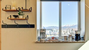 Uma cozinha com vista pela janela, cafeteira e prateleiras com diversos objetos.