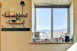 Eine Küche mit Fensterblick, einer Kaffeemaschine und Regalen mit unterschiedlichen Gegenständen.