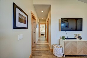 Un couloir avec un plancher en bois, un téléviseur fixé au mur et un lit visible au loin.
