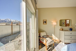 Une chambre d’hôtel dotée d’une porte-fenêtre coulissante, d’une chaise, d’une table de chevet avec une lampe, d’une commode et offrant une vue sur des montagnes enneigées.