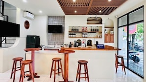 Un espace bar moderne avec des tabourets en bois, un comptoir agrémenté d’une enseigne et une vue sur l’extérieur.