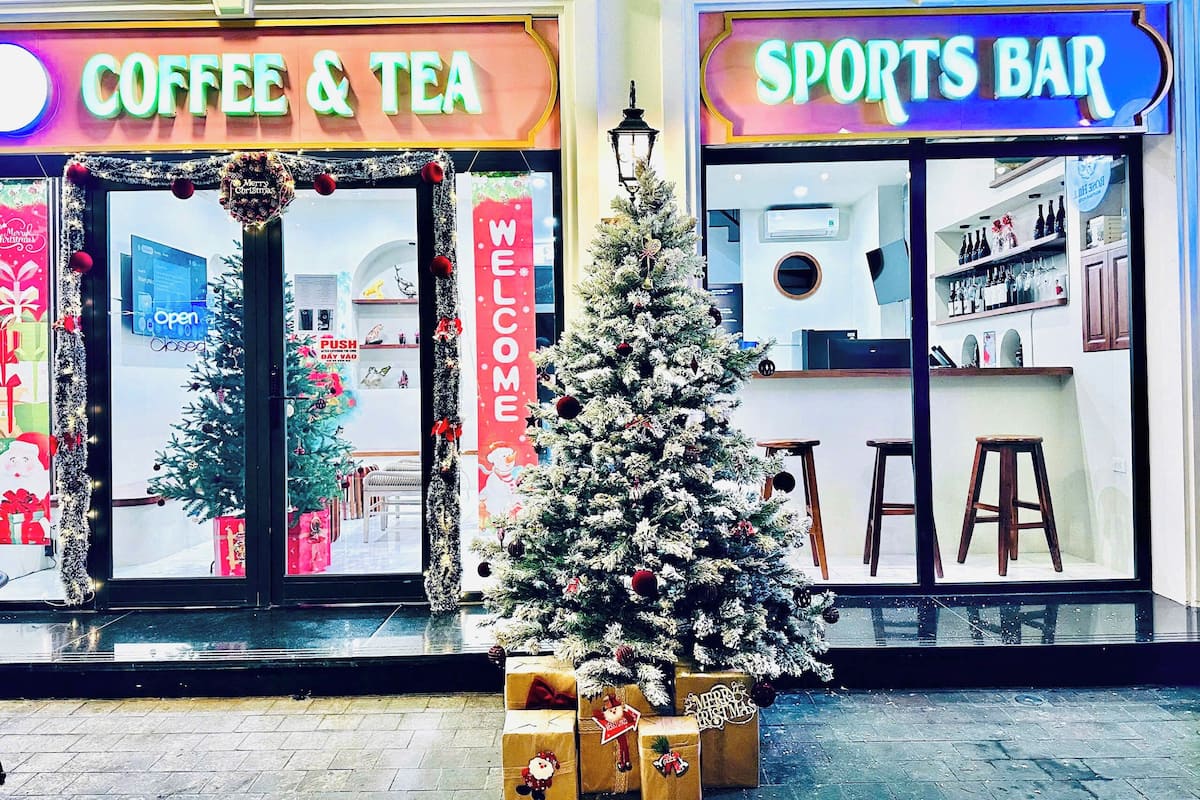 Ein Schaufenster mit einem Weihnachtsbaum und Geschenkkartons, einem Schild mit der Aufschrift 'Coffee & Tea' und einem Schild mit der Aufschrift 'Sports Bar'.