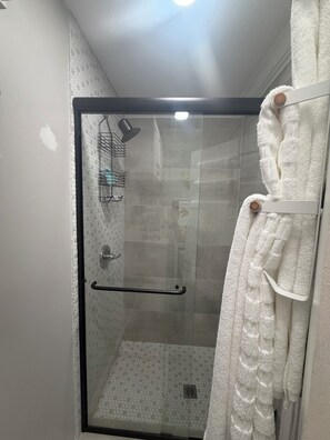 Eine begehbare Dusche mit Glastrennwand, Handtuchhalter, Duschkopf und einer Glastür.