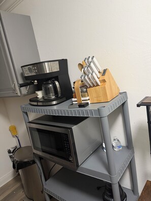 Eine Küchenzeile mit einer Kaffeemaschine, einer Mikrowelle und einem Messerblock auf einer grauen Arbeitsplatte.