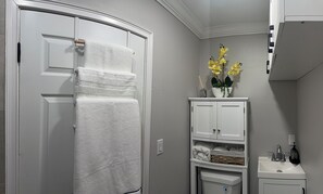 Ein Badezimmer mit einer weißen Tür, einem weißen Schrank mit Waschbecken und einem Blumentopf mit gelben Blüten.