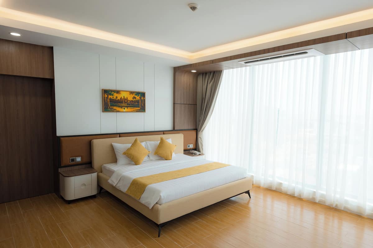 Une chambre d’hôtel moderne avec un grand lit, des lambris en bois, un tableau au mur et une grande fenêtre ornée de rideaux légers.