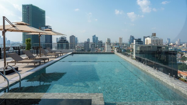 Une piscine à débordement située sur le toit, avec des chaises longues et des parasols, offrant une vue imprenable sur le paysage urbain.
