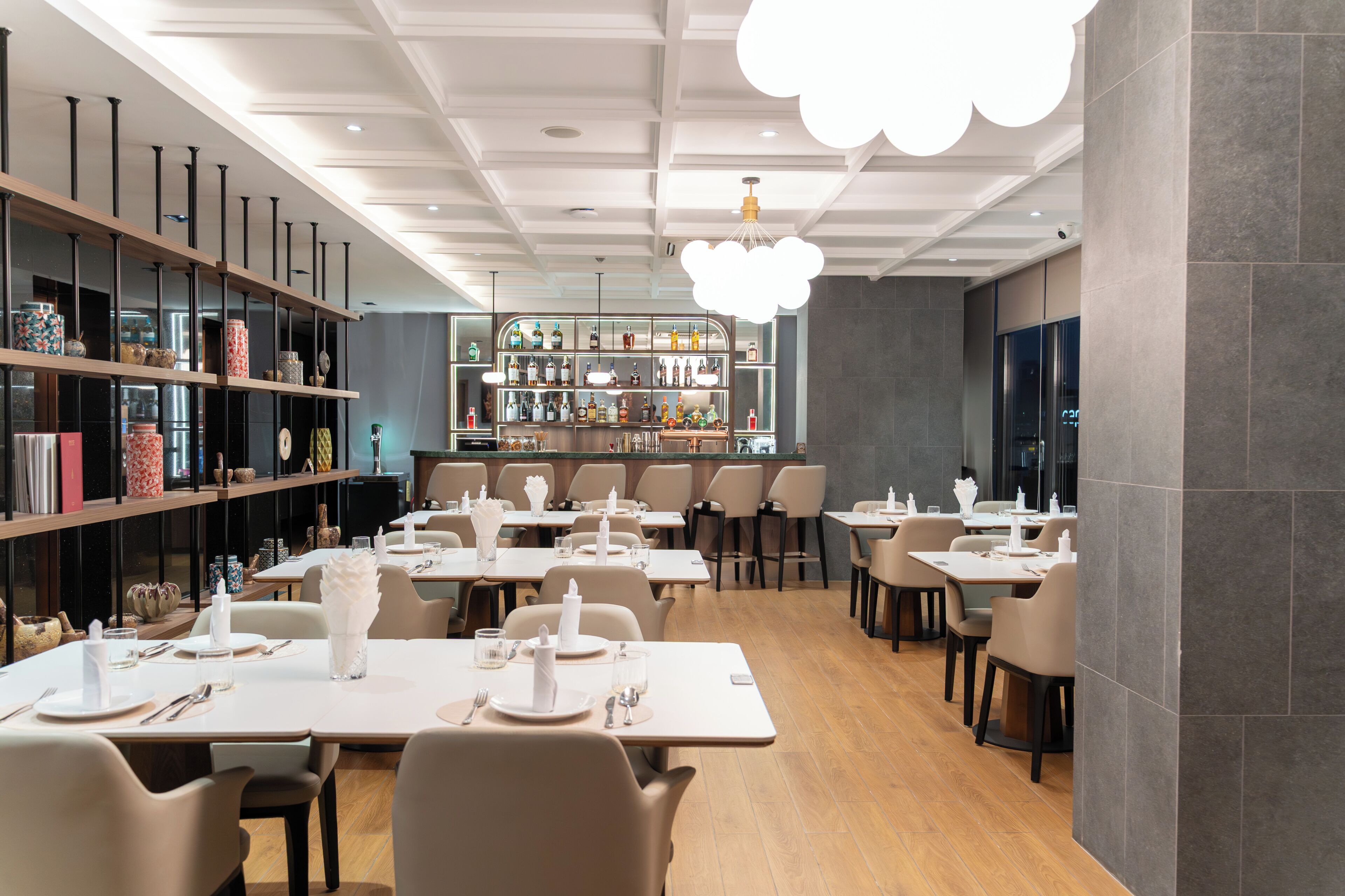 A modern restaurant interior with multiple dining tables, chairs, and a bar area.