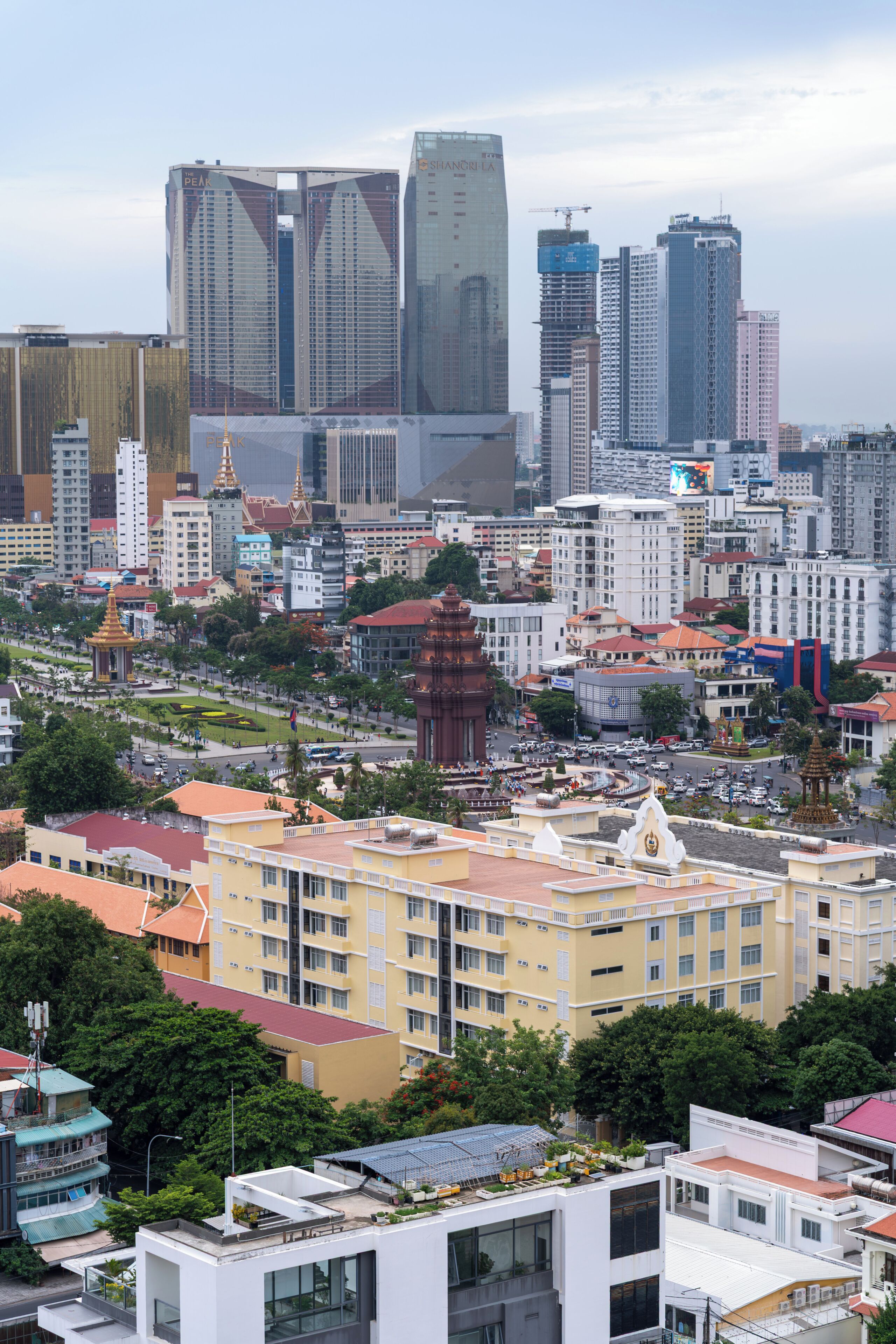 A cityscape with modern high-rise buildings, a central plaza with a monument, and surrounding residential buildings.