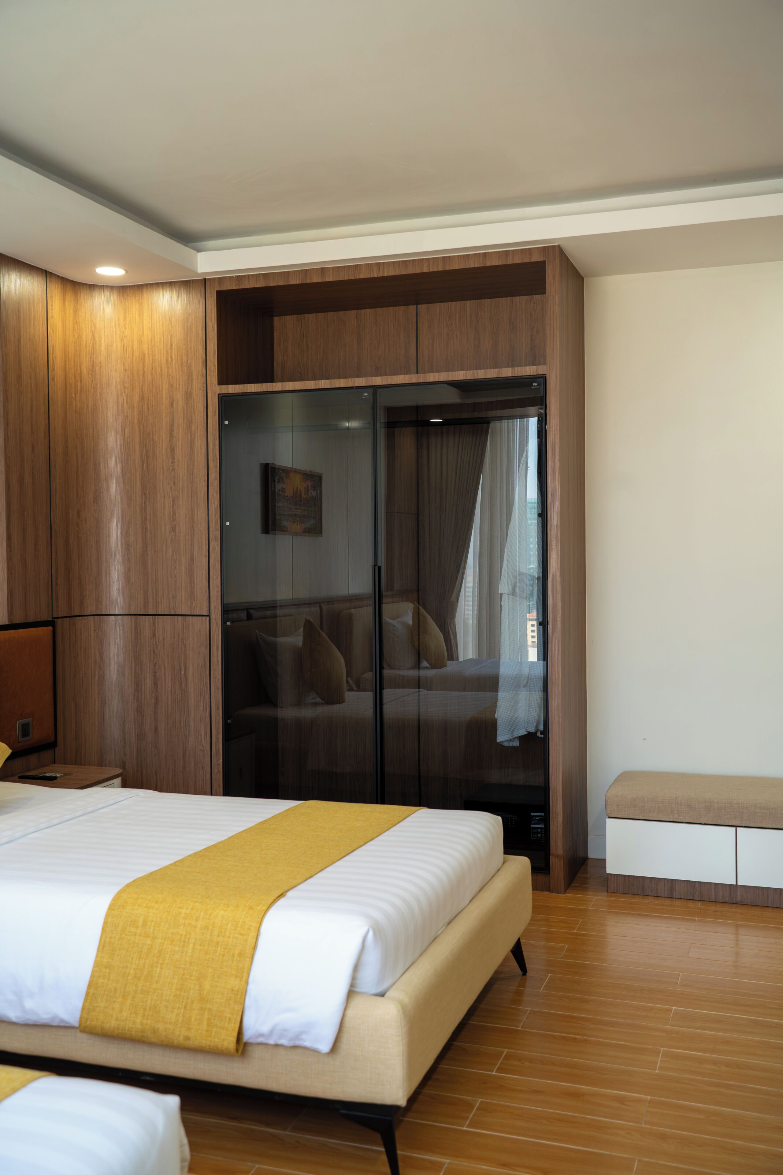 A hotel room with a large bed, a wardrobe, a seating area, and a glass door leading to a balcony.