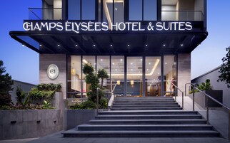 Entrada de hotel con una escalera que conduce a las puertas, un letrero sobre la entrada y un logotipo en la pared.