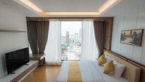 Une chambre d’hôtel moderne avec un grand lit, un téléviseur posé sur une étagère intégrée et une vue sur la ville par la fenêtre.
