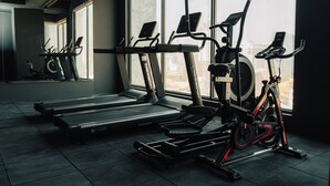 Une salle de sport équipée de matériel d’exercice, dotée de grandes fenêtres et offrant une vue sur les bâtiments.
