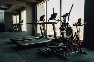 Un gimnasio con equipo de ejercicio, amplias ventanas y vistas a edificios.