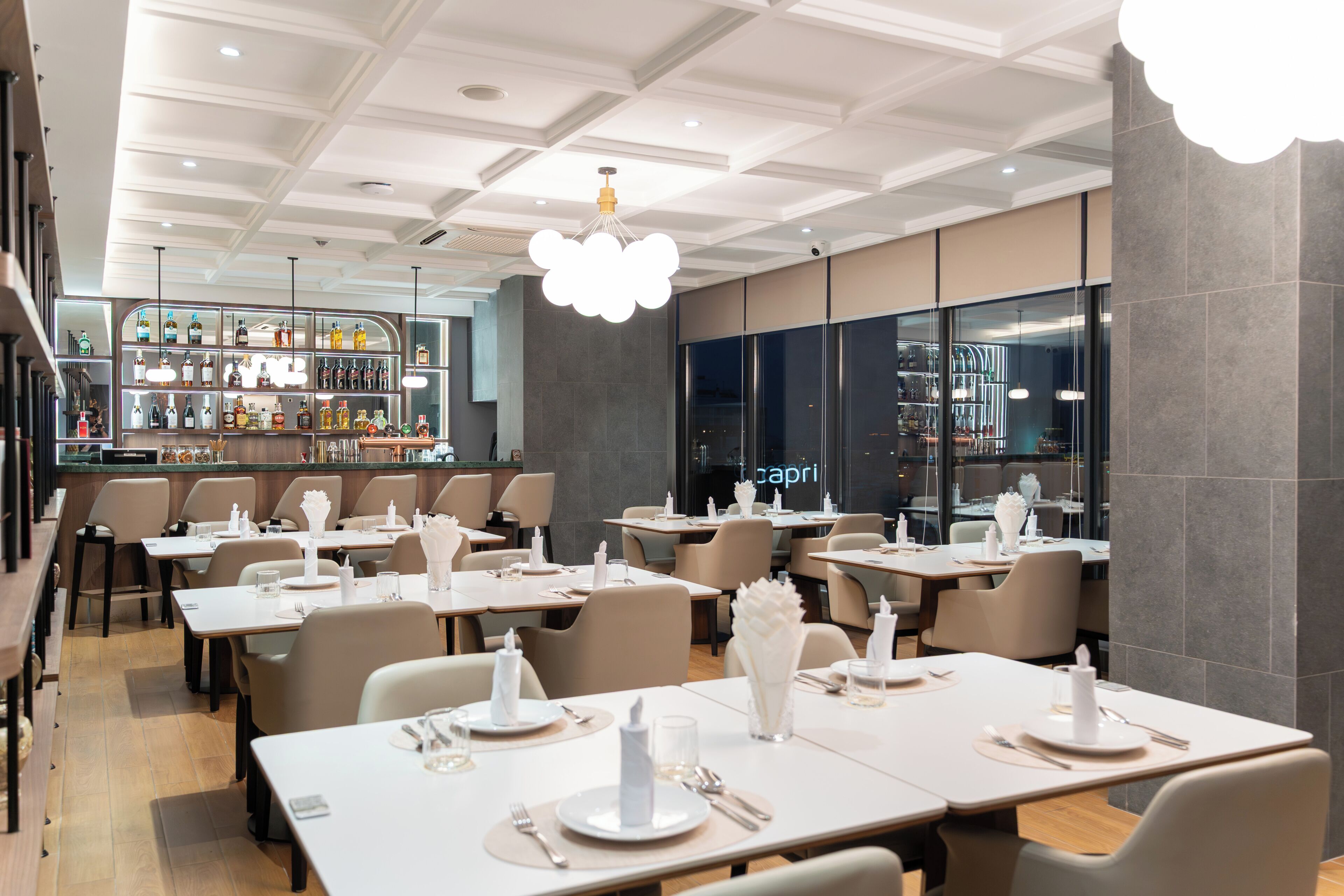 A modern restaurant with a bar area, neatly arranged tables, and a contemporary ceiling design.