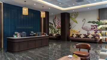 Un área de recepción moderna con pared azul, mostrador de recepción y zona de estar con sofás y una mesa de madera.