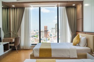 Habitación de hotel con cama, escritorio y silla. Cuenta con un ventanal con cortinas y vistas a la ciudad.
