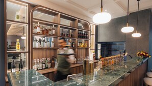 Un espace bar doté d’un comptoir en marbre, d’étagères remplies de bouteilles d’alcool et de luminaires suspendus.