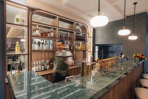 Una zona de bar con mostrador de mármol, estantes con botellas de licor e iluminación colgante.