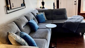 En moderne stue med en hjørnesofa, et rundt sofabord og et stort spejl.