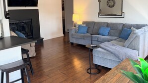 En moderne stue med sofa, fjernsyn, pejs og loftventilator.