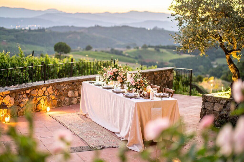 An outdoor dining area with a table set for a meal, surrounded by stone walls and a scenic view of rolling hills.
