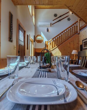 A dining area with a long table set for a meal, wooden walls, a staircase, and a small decorative plant. - Longs Newly Remodeled Cabin with King Suite • 23 Miles to Yellowstone (Island Park)
