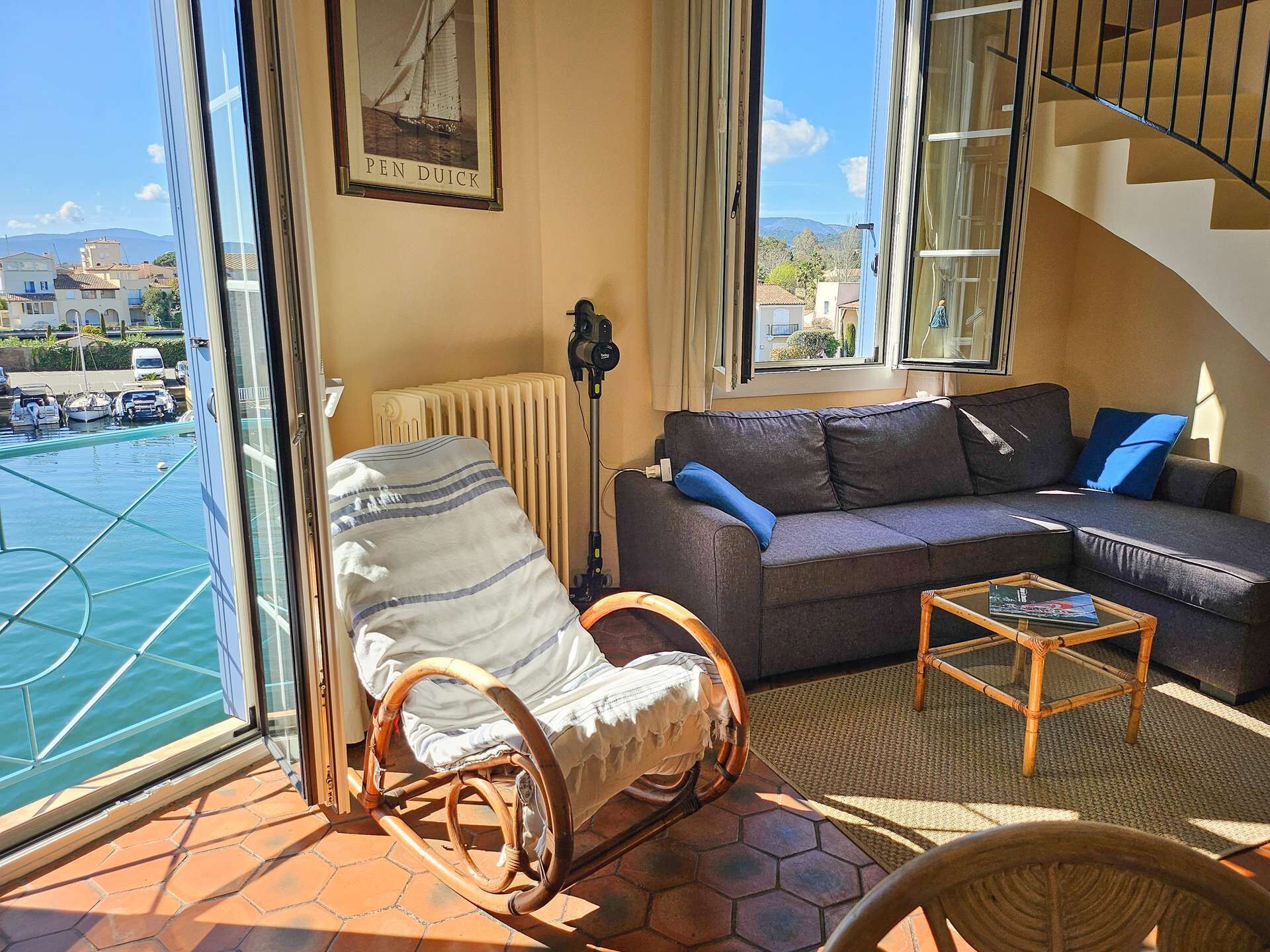 A balcony with a view of a marina, a sofa, a rocking chair, and a small table.