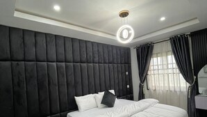 A modern bedroom with a large bed, a bedside table, and a ceiling light fixture. - J3's Apartment & Lounge (Benin City)