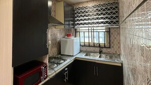 A compact kitchen with dark cabinetry, a microwave, a stove, and a window with patterned curtains. - J3's Apartment & Lounge (Benin City)