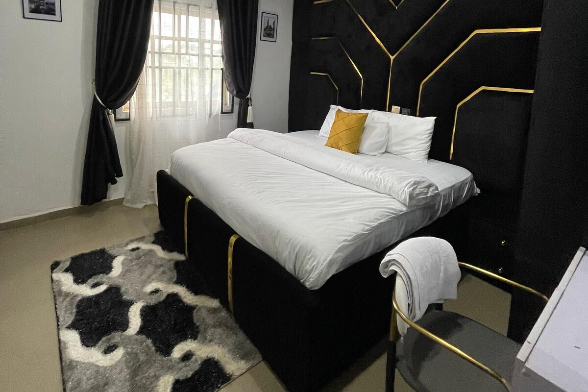 Une chambre moderne avec un grand lit, un mur d’accent aux couleurs noir et or, une tête de lit noire et une petite table de chevet.