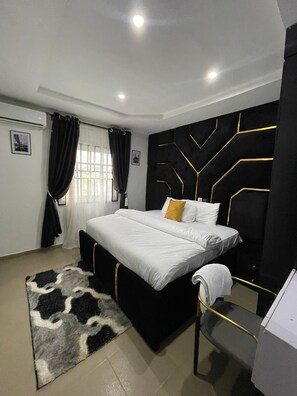 A modern bedroom with a large bed, a black and gold accent wall, a black headboard, and a small bedside table. - J3's Apartment & Lounge (Benin City)