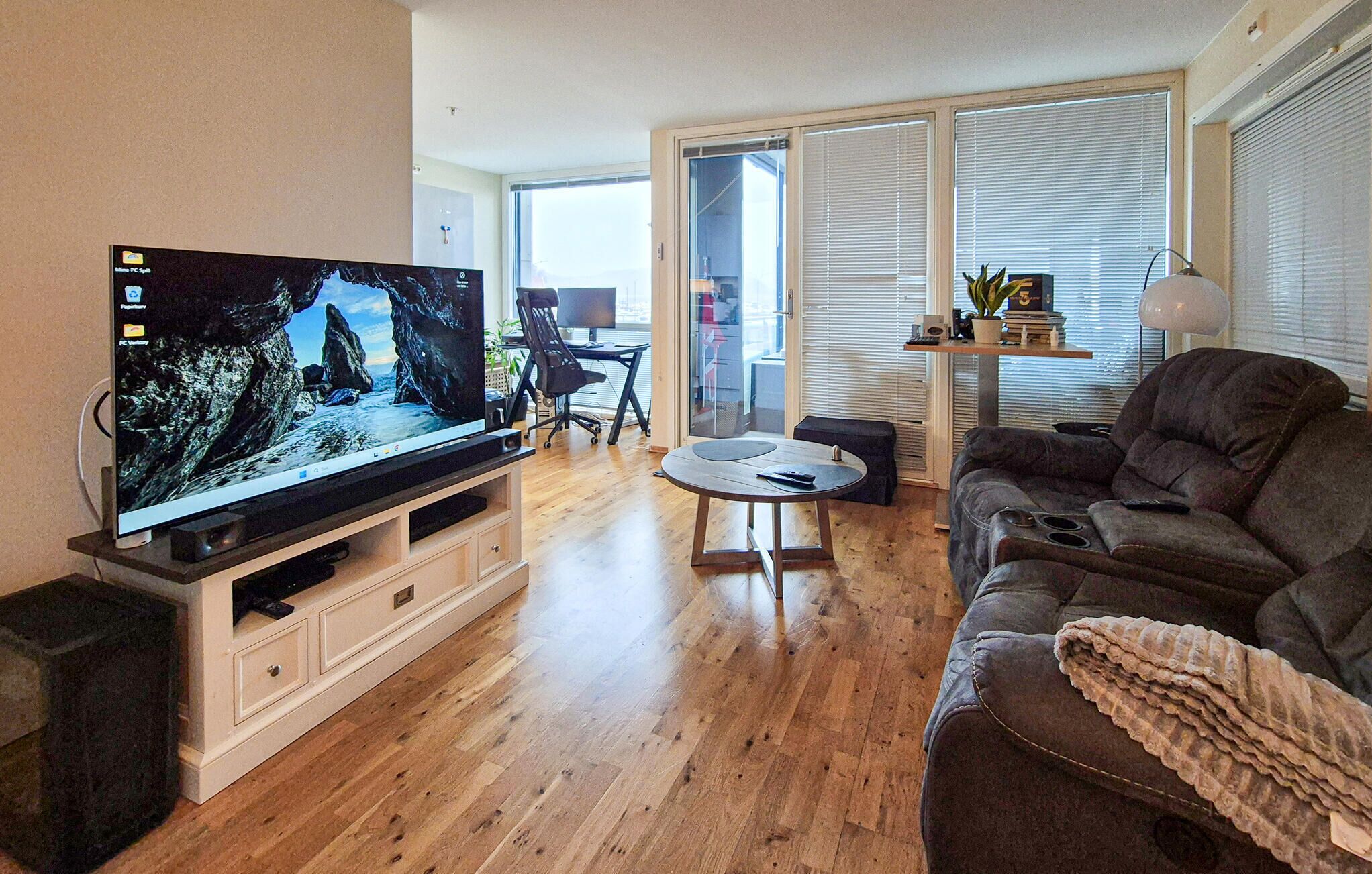 A living room with a flat-screen TV, a sofa, a coffee table, and a sliding glass door leading to a balcony.