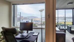 Quarto moderno com uma janela ampla, uma escrivaninha com computador e vista para um porto de iates.