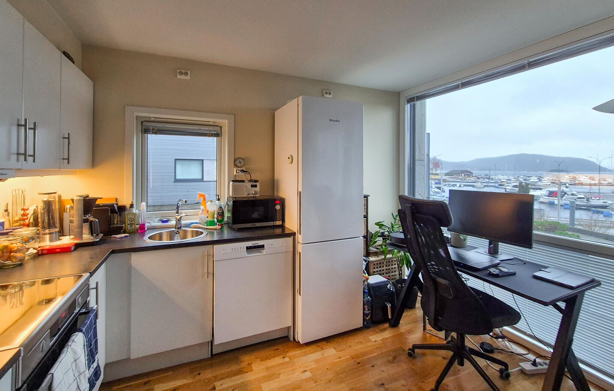 A compact kitchen with a microwave, toaster, and sink. There's a window with a view of a marina and mountains.