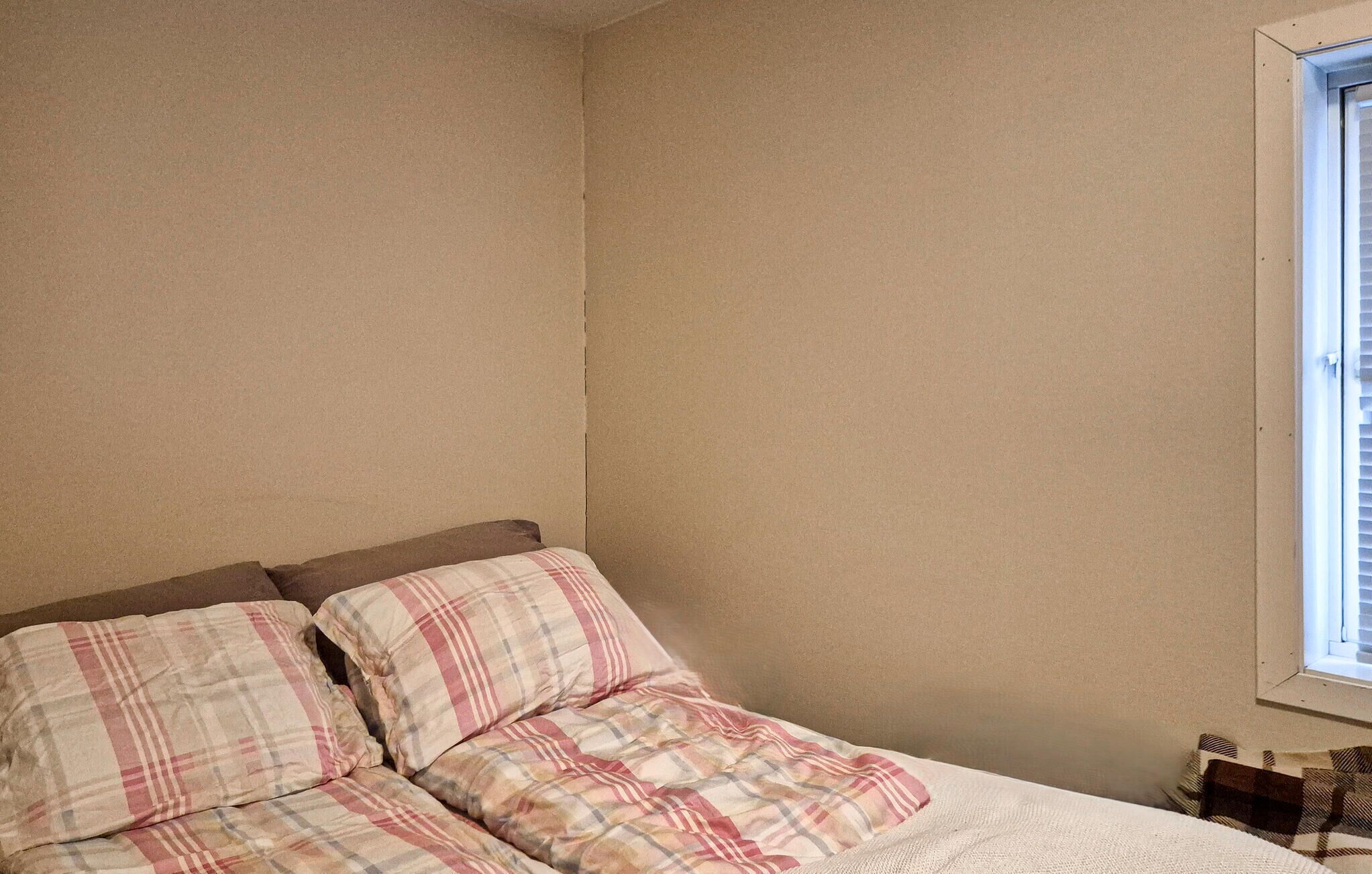 Une chambre à coucher avec un lit, des oreillers, une fenêtre et un mur.