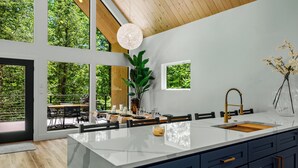 Eine moderne Küche mit einer großen Kochinsel, Holzboden und großen Fenstern mit Blick auf Grünflächen.
