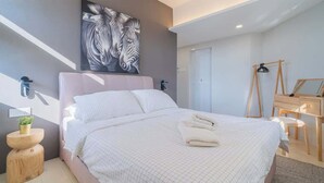 Un dormitorio moderno con una cama grande, una mesita de noche de madera con una planta, un escritorio con una silla y una obra de arte con estampados de cebra en la pared.