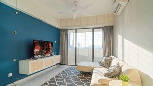 Una sala de estar moderna con televisión de pantalla plana, ventilador de techo, sofá y un ventanal con cortinas.
