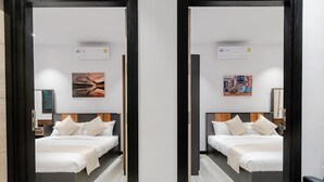 Een spiegelbeeld van een hotelkamer met een bed, kussens, een nachtkastje, een wandairconditioner en kunstwerk.
