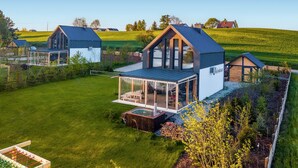 A modern house with a large glass conservatory, a wooden deck, and a surrounding garden.