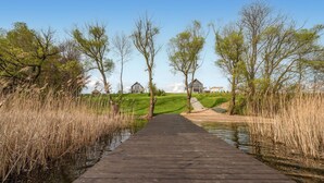 A wooden pathway leading to a building with a modern design, surrounded by grassy areas and trees.