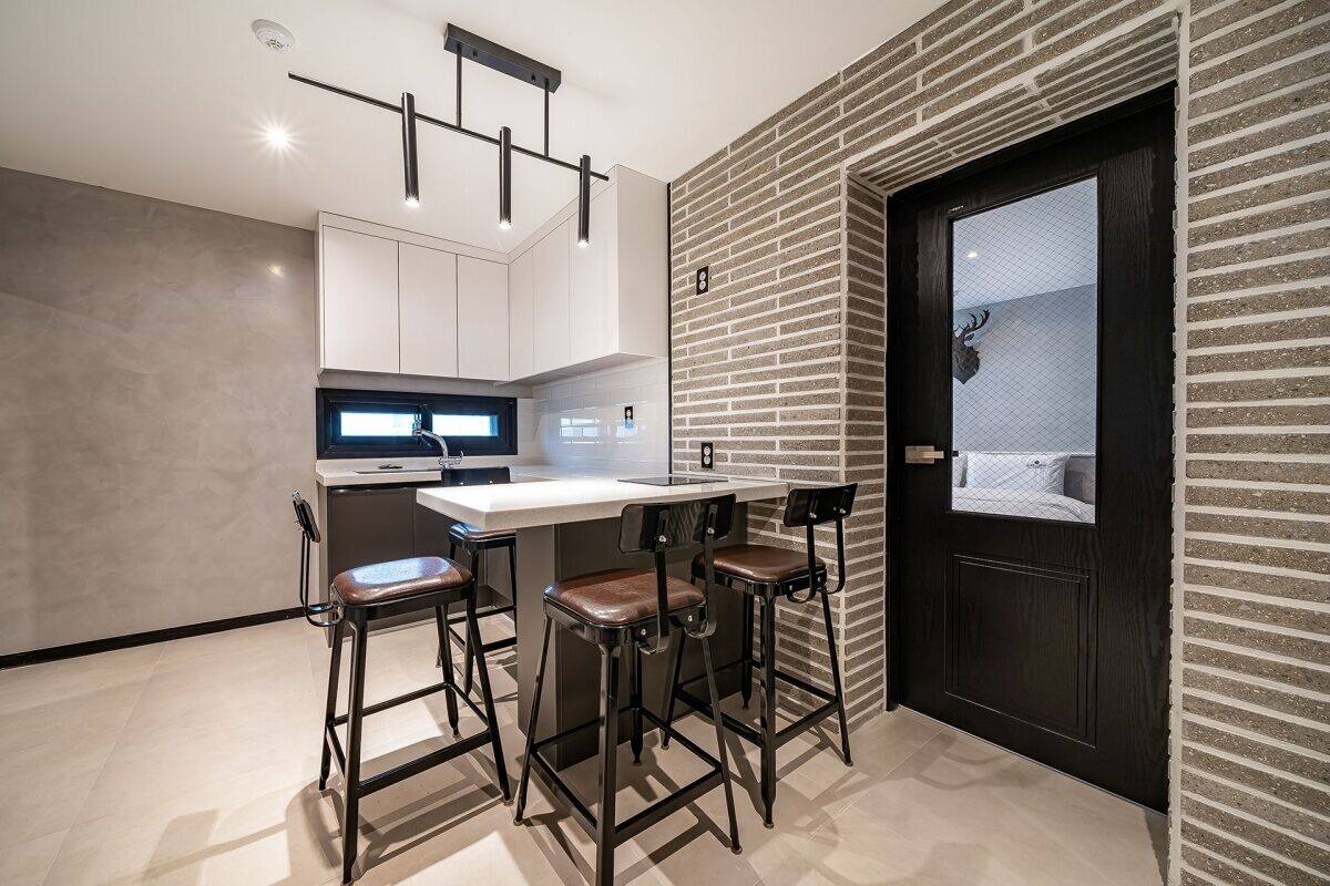 A modern kitchen with white cabinets, a black countertop, and three bar stools.