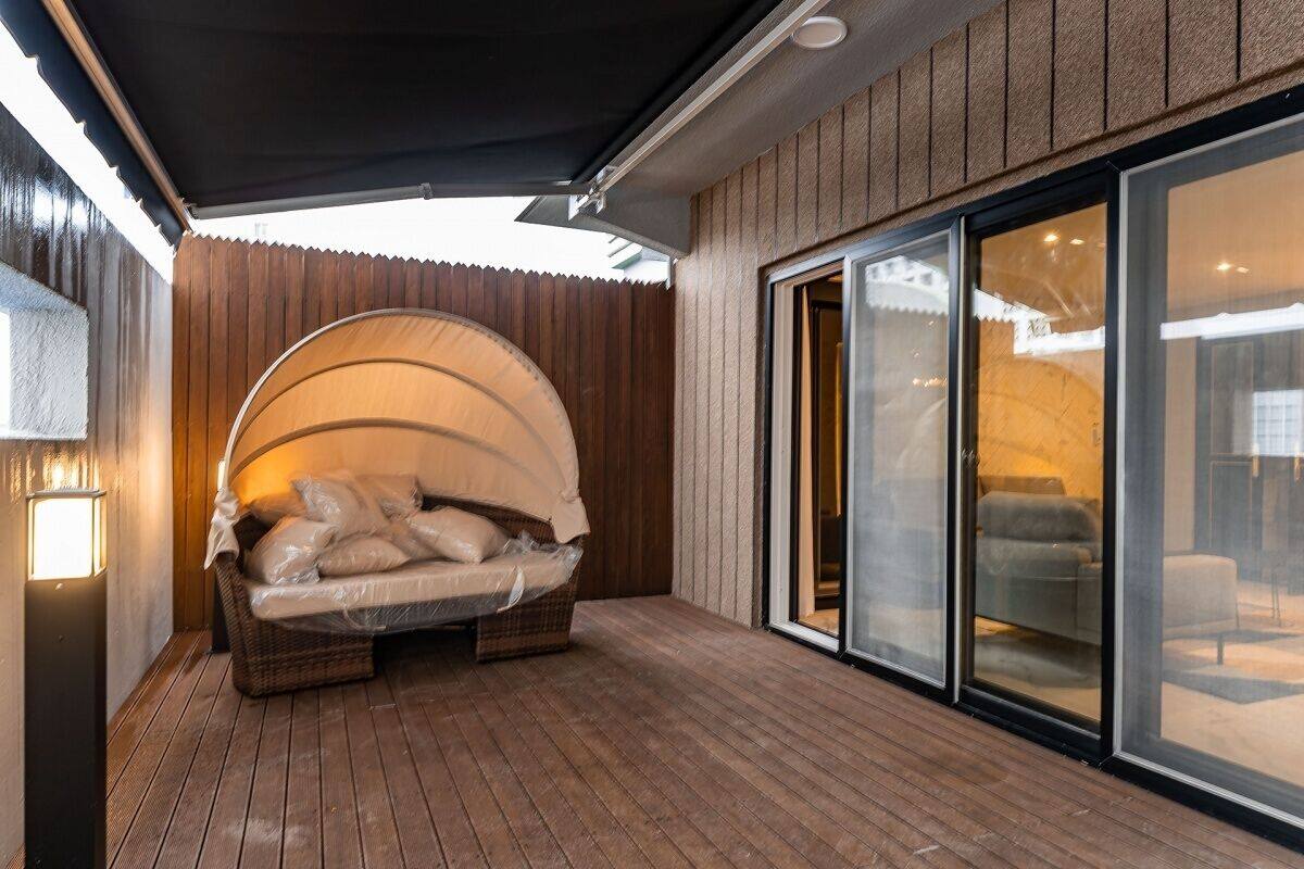 A covered patio area with a cushioned seating arrangement, a wooden deck, and a sliding glass door leading to an interior space.